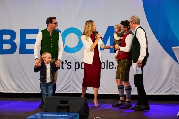 Johannes und Roman Bock stehen gemeinsam mit ihren Familien und Moderatorin Sissy Gamauf-Leitner auf der Bühne der Jubiläumsfeier zu 40 Jahren BECOM.