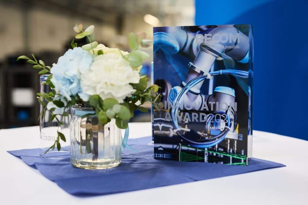Becom Innovation Award 2025 1 Die gläserne Trophäe des BECOM Innovation Award 2025 dekoriert auf einem Tisch mit Blumenschmuck.
